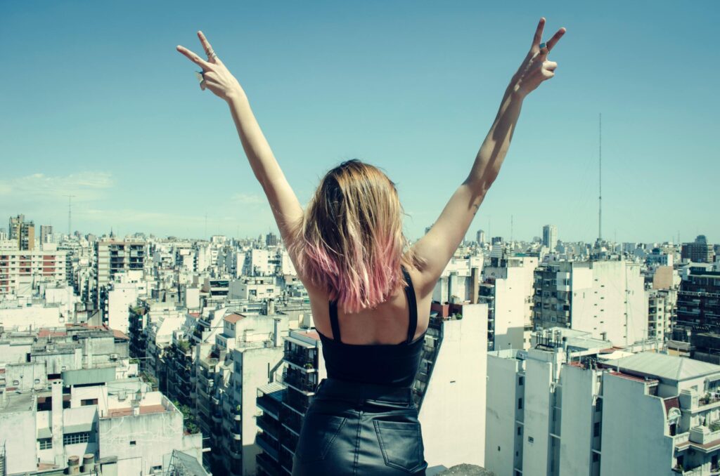 Woman Standing on Rooftop Putting Hands in the Air Under Clear Sky
